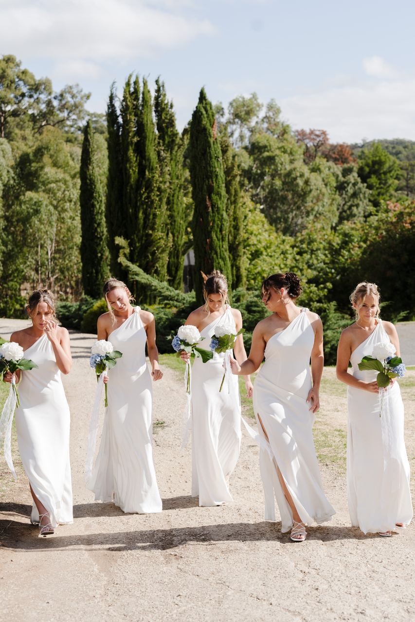 The bridesmaids walking down the gravel drive in white