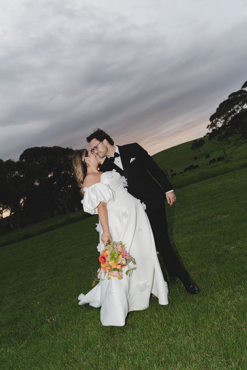 Zak and Zoe kissing at dusk, bouquet in hand