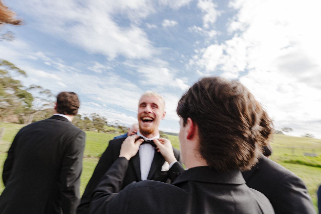 A groomsman laughing as his bow tie is straightened