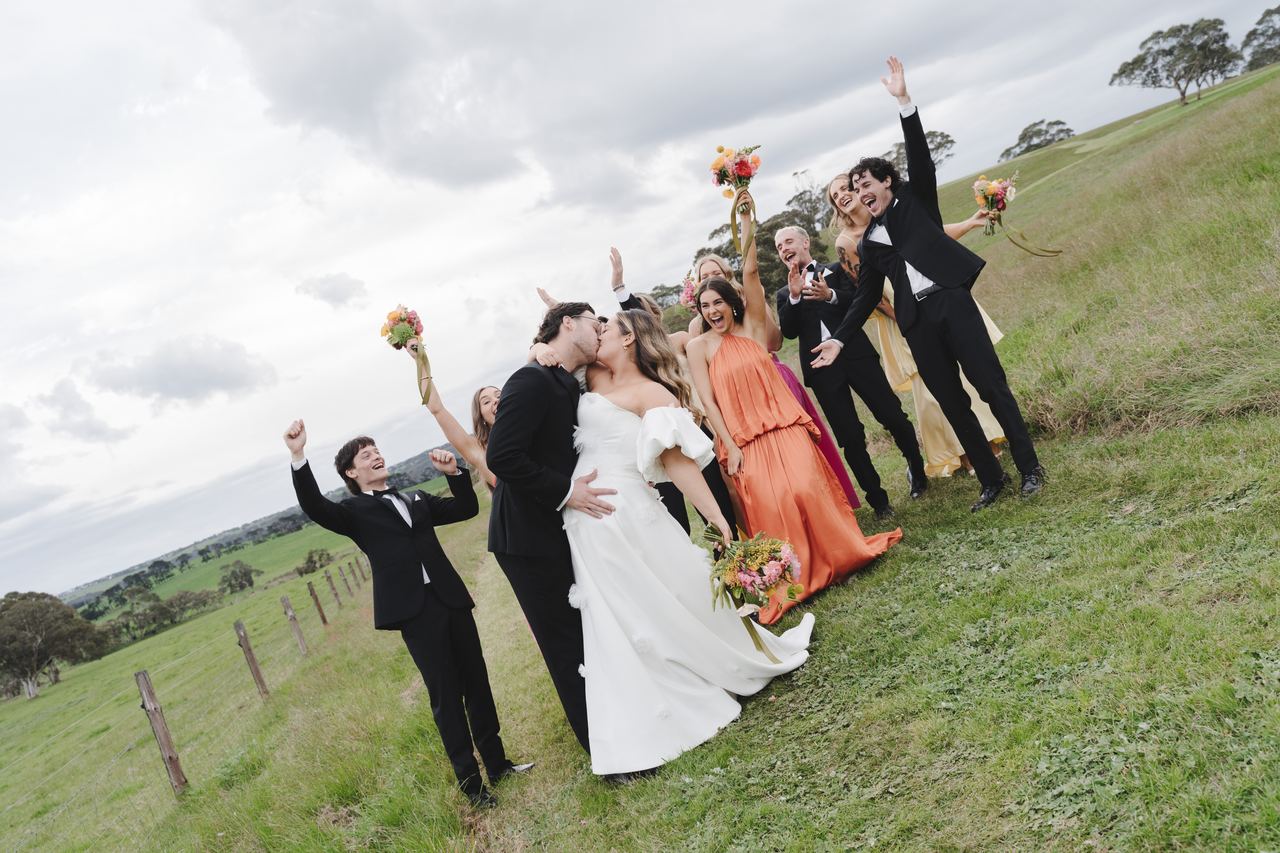 The wedding party cheering around Zak and Zoe in the paddock