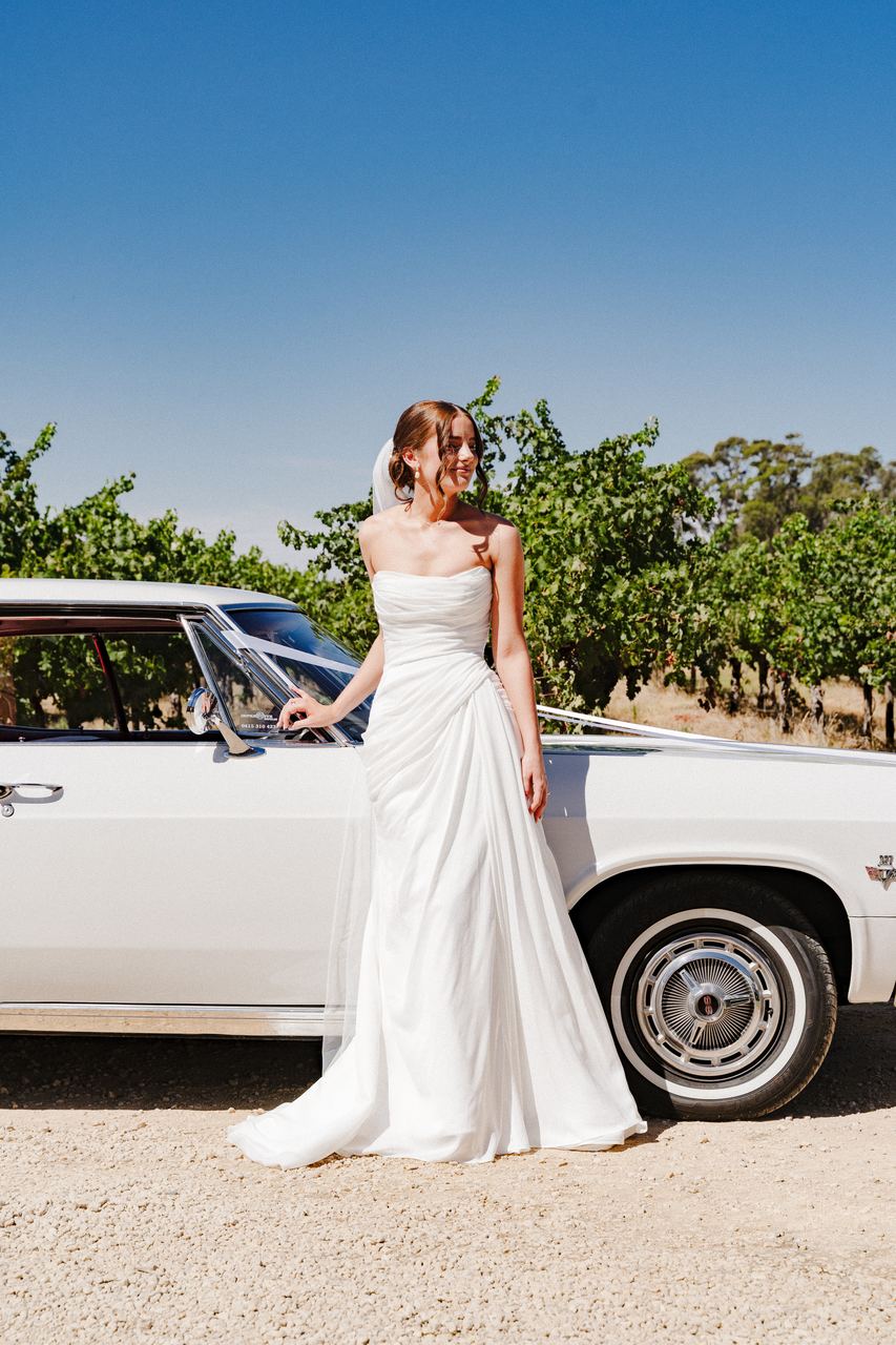 Emma beside a vintage car among the vines