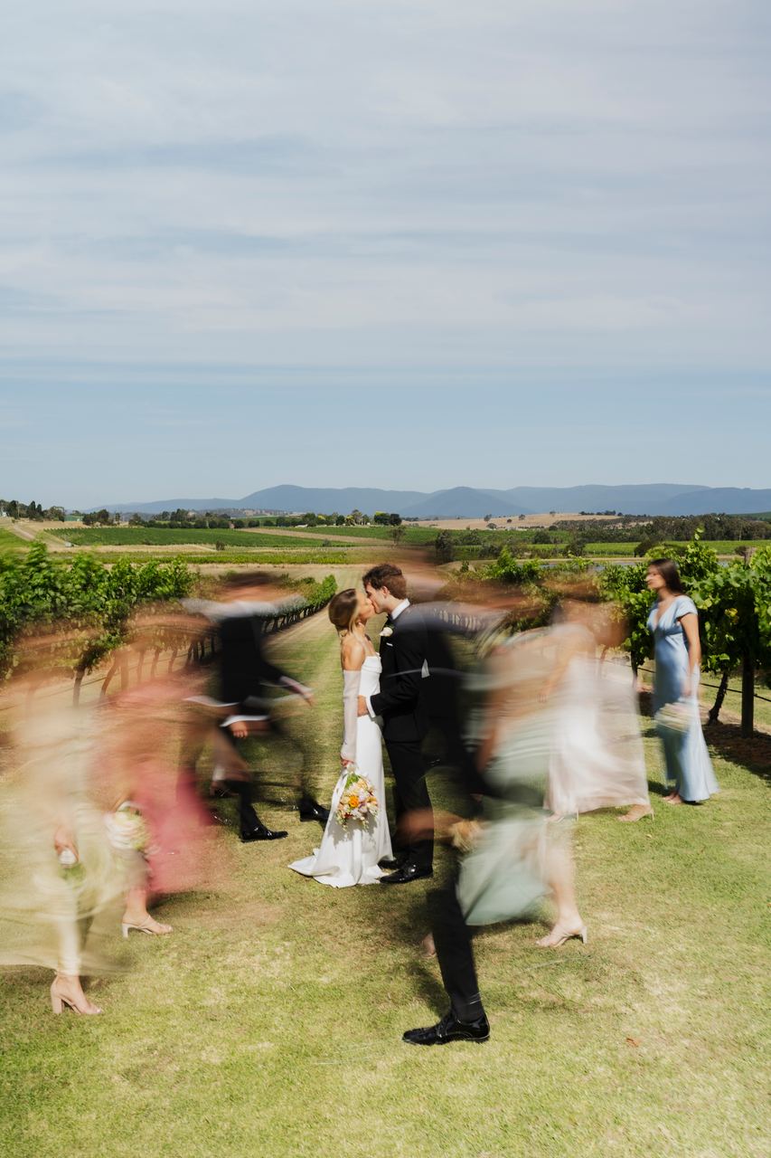 Caleb and Georgia in the vineyard as the wedding party moves past
