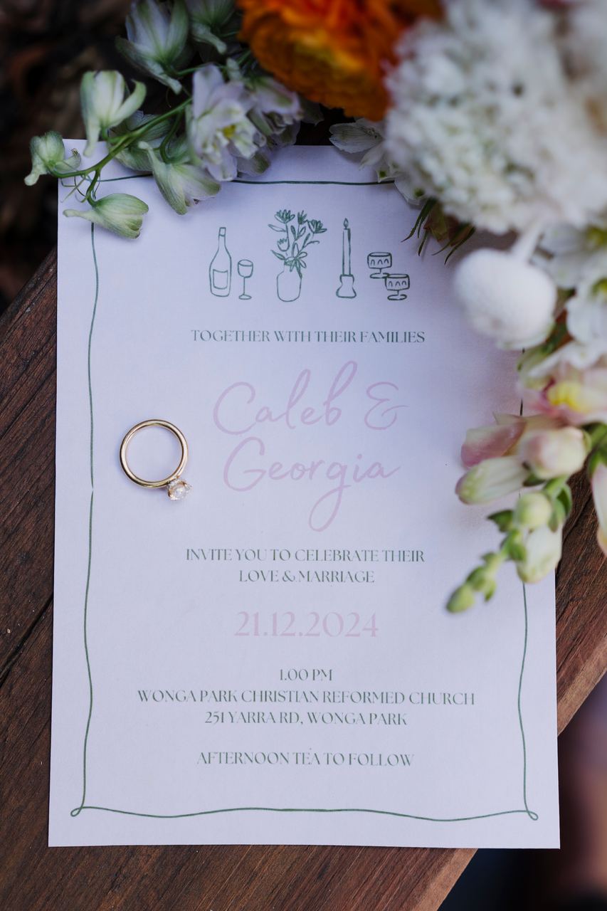 Caleb and Georgia's invitation with the rings and flowers